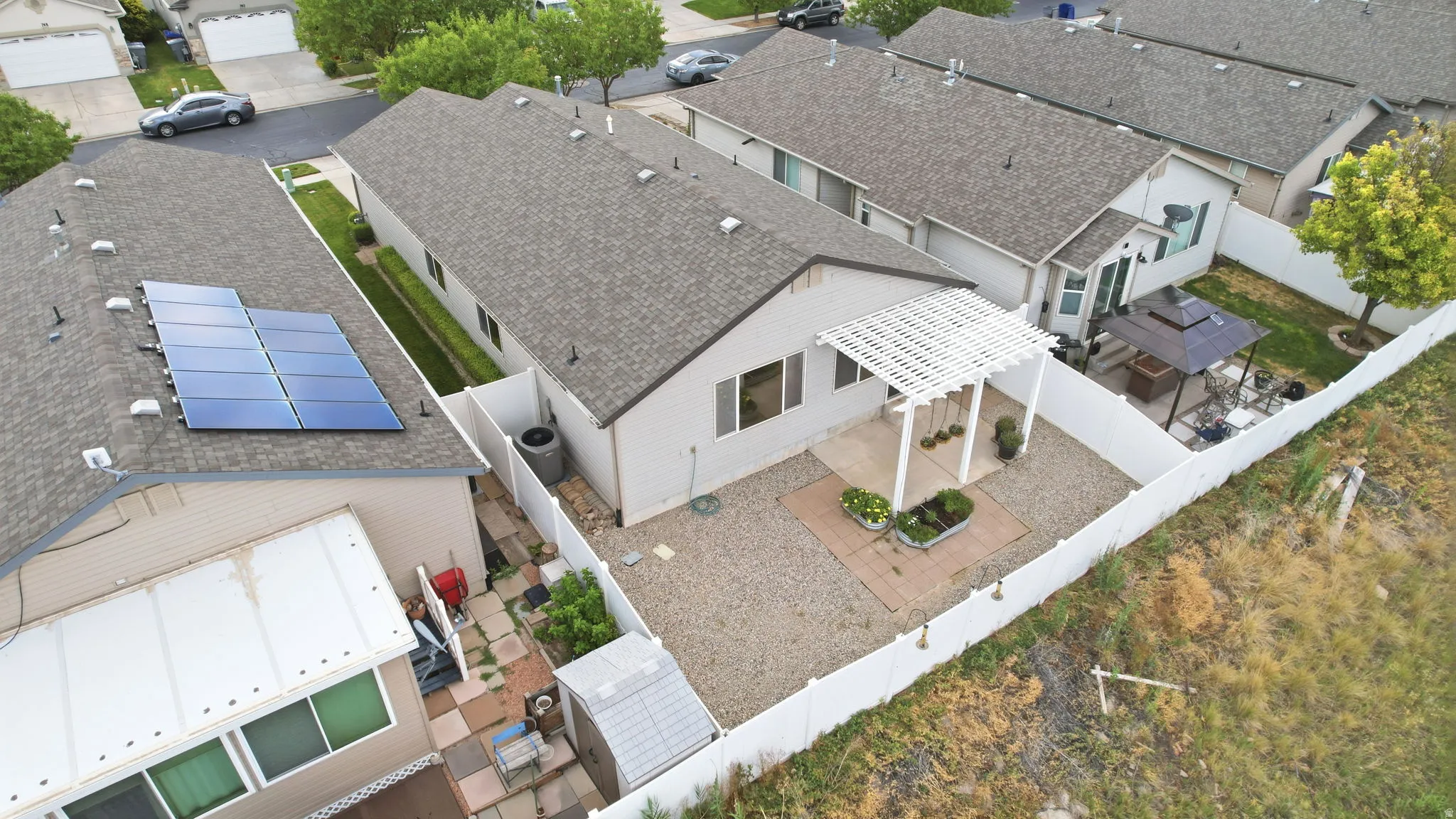 Low-maintenance backyard featuring a white lattice pergola, gravel patio area, privacy fencing, and a separate paved side yard