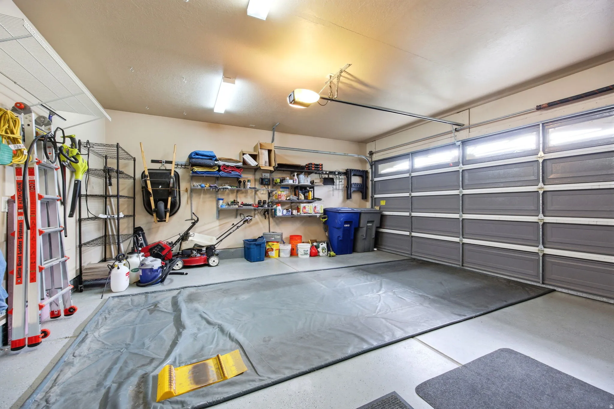 Spacious garage with an automatic overhead door, overhead lighting, an epoxy-coated floor, and built-in shelving systems