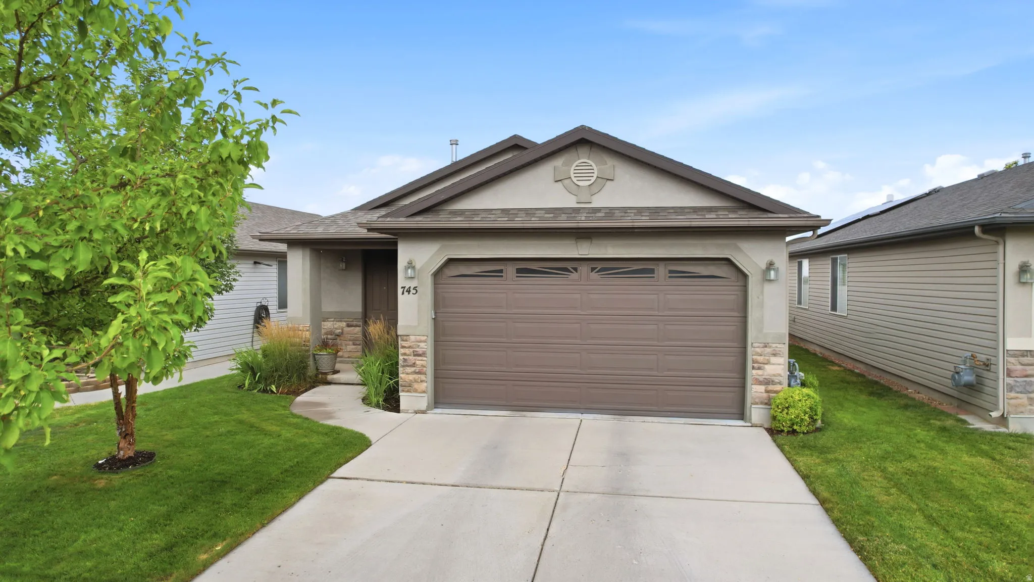 Ranch-style exterior featuring a two-car garage, stone and stucco facade, concrete driveway, and established landscaping