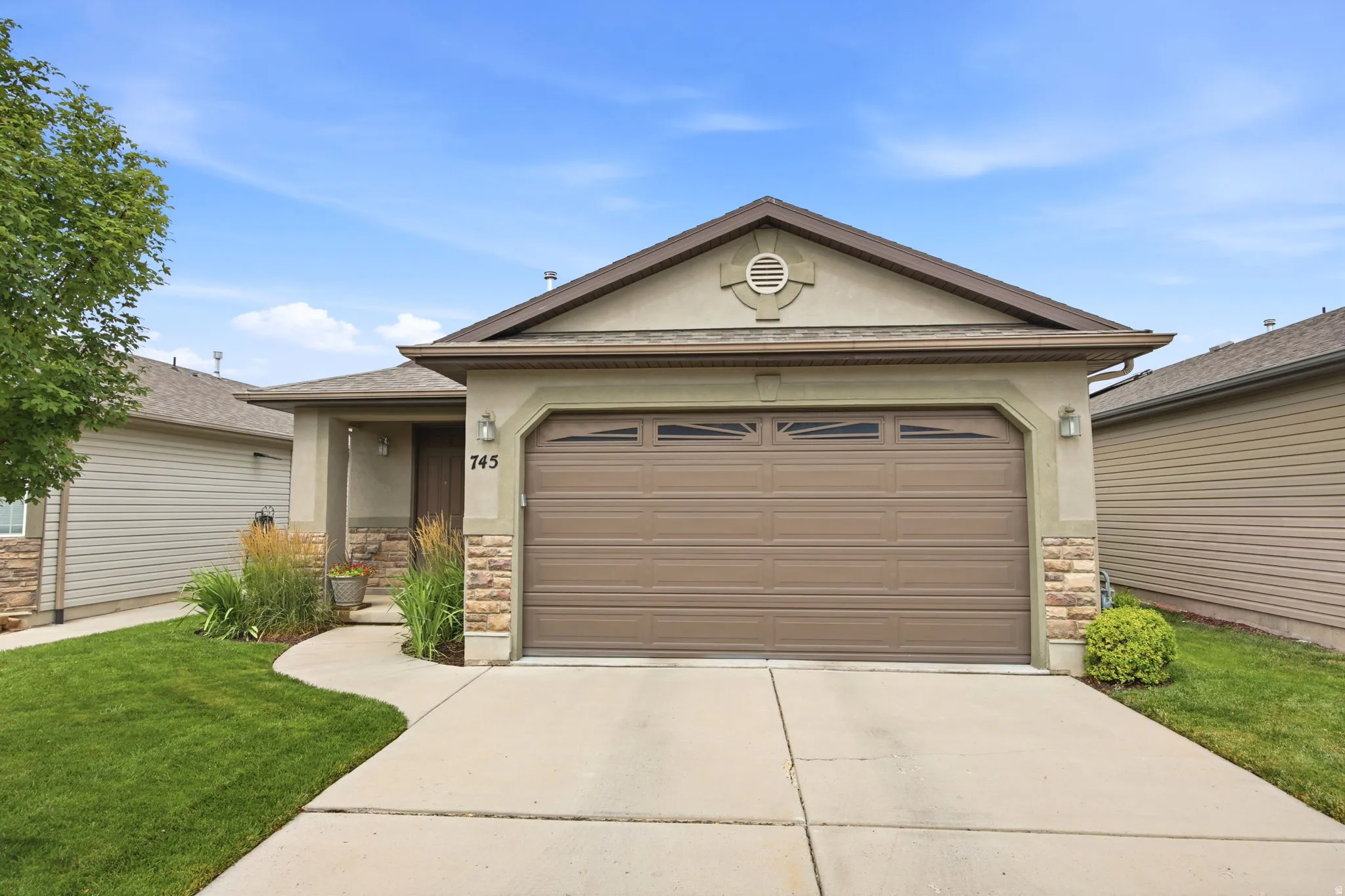 Exterior facade featuring a brown garage door with window inserts, stucco siding, and stone accents