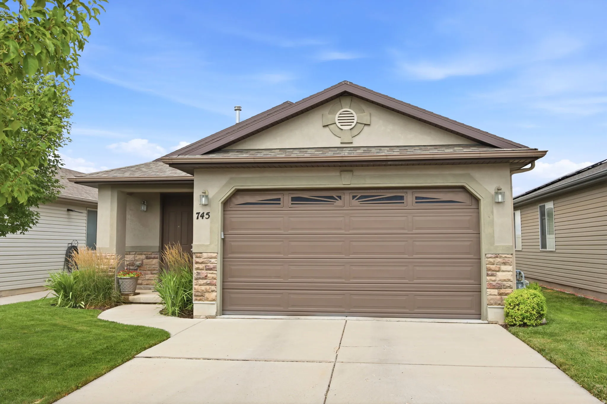 Front exterior with a two-car garage, stone façade accents, stucco siding, a covered entry, and a concrete driveway