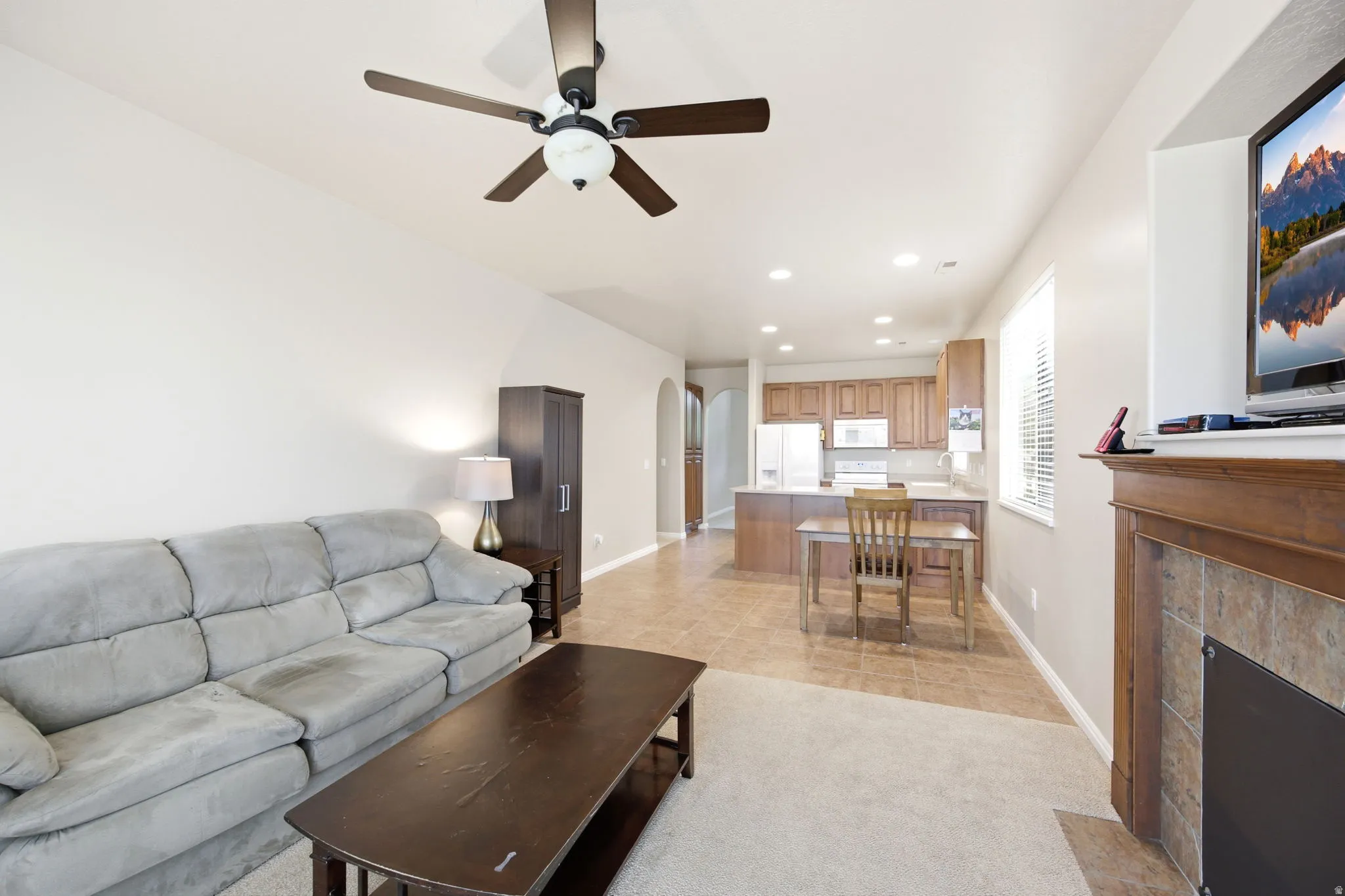 Living area featuring a fireplace with a wood-finish mantel and tile surround, accompanied by an overhead ceiling fan