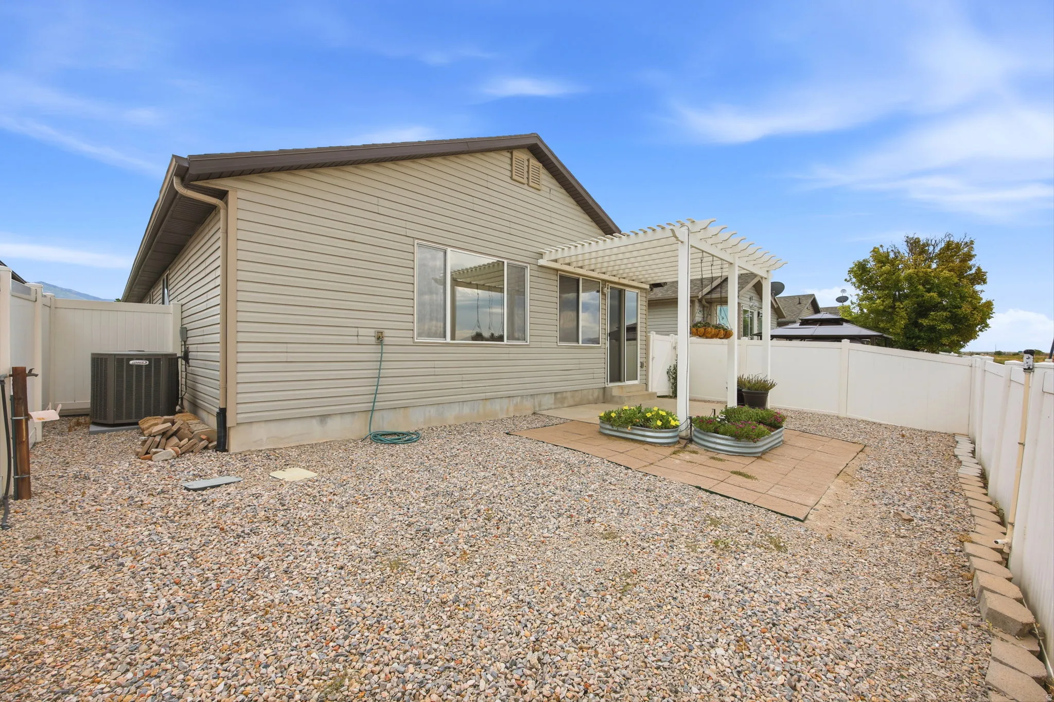 Rear exterior featuring a stone-covered yard, white vinyl fencing, and a patio with a white pergola