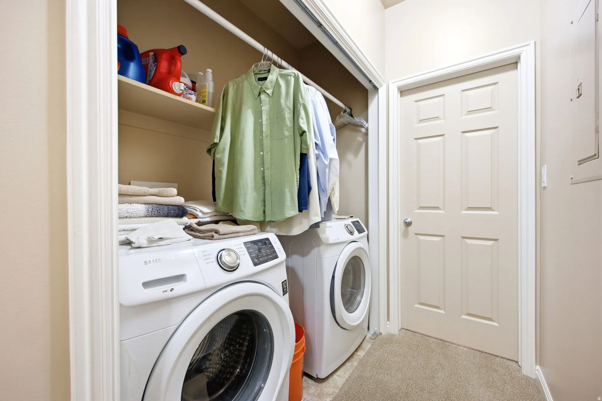 Dedicated laundry area featuring a built-in shelf, clothing rod, and neutral-toned carpet flooring