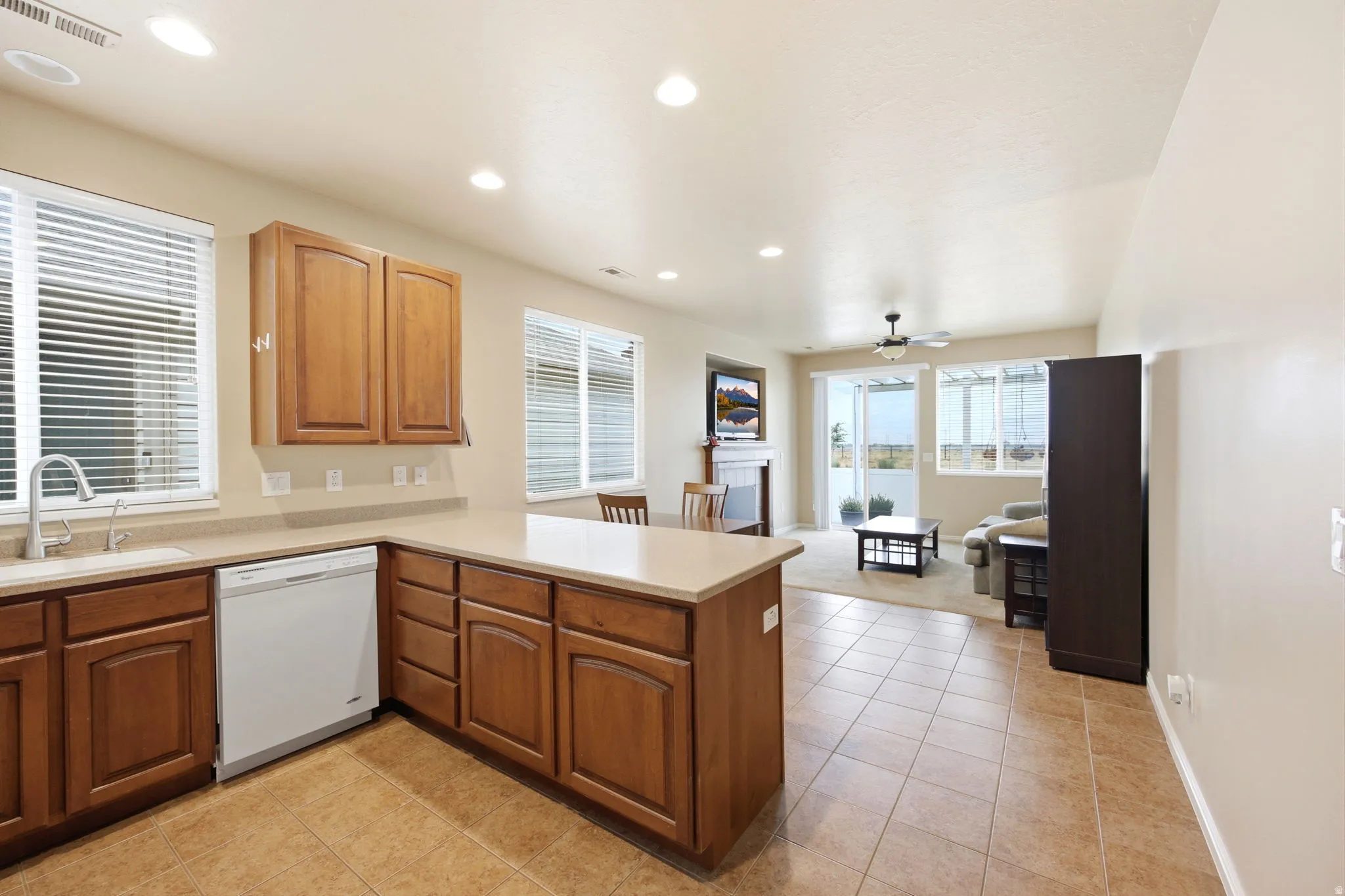 Open concept kitchen featuring warm wood cabinetry, light-toned countertops, and tile flooring