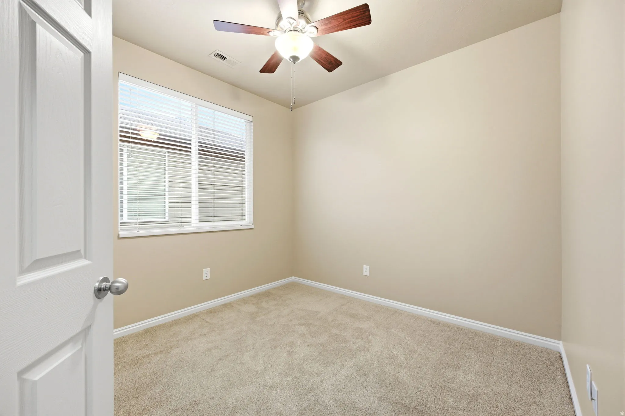 Neutral-toned room featuring a window with blinds, carpet flooring, and a ceiling fan with integrated lighting