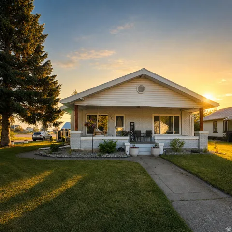 Single-story residence featuring a covered front porch with brick pillars and siding, a concrete pathway, a manicured lawn, and mature landscaping
