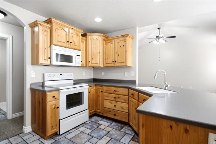 Well-appointed kitchen featuring light wood cabinetry, white appliances, dark countertops, and tile flooring