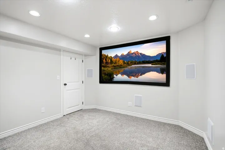 Dedicated media room featuring a large projection screen, recessed lighting, and wall-mounted speakers