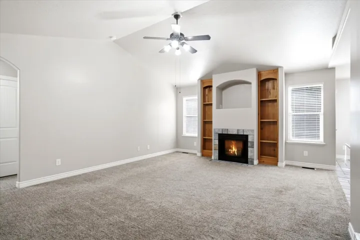 Spacious living area featuring a vaulted ceiling and a ceiling fan with integrated lighting