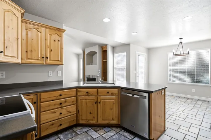 Kitchen featuring wood cabinetry, dark countertops, a stainless steel dishwasher, and recessed lighting