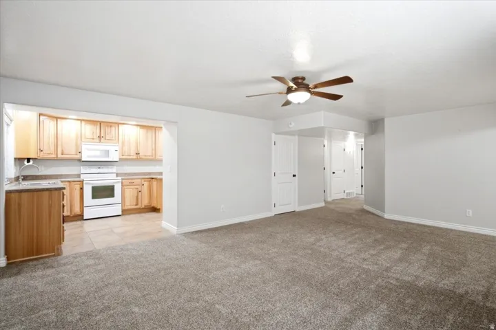 Open-concept living space featuring a ceiling fan with integrated lighting, neutral wall tones, and plush carpeting