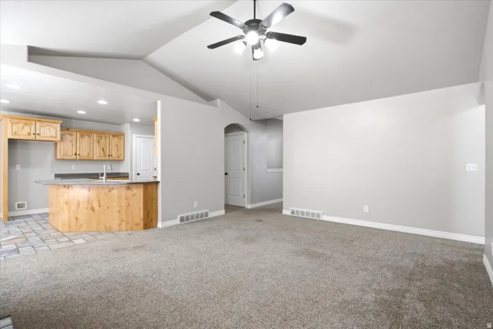 Spacious living area featuring vaulted ceilings, a ceiling fan, and carpet flooring