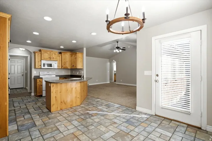 Kitchen featuring light wood cabinetry, white appliances, a peninsula with a dark countertop, recessed lighting, and multi-toned tile flooring