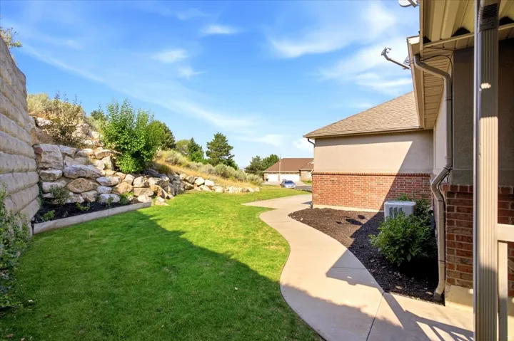 Exterior property side yard featuring a retaining wall, sloped rock landscaping, and a curvilinear paved path