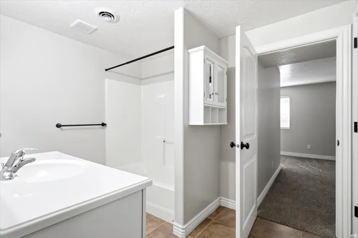 Bathroom featuring a white vanity with integrated sink, chrome faucet, white shower/tub combination with black shower rod, and tan tile flooring