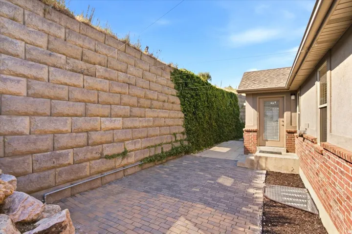 Paver patio area with a stone retaining wall and mature greenery
