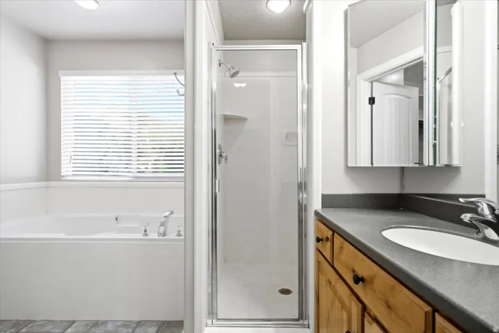 Bathroom featuring a white soaking tub with window, glass-enclosed shower, wood vanity with integrated sink, and medicine cabinet