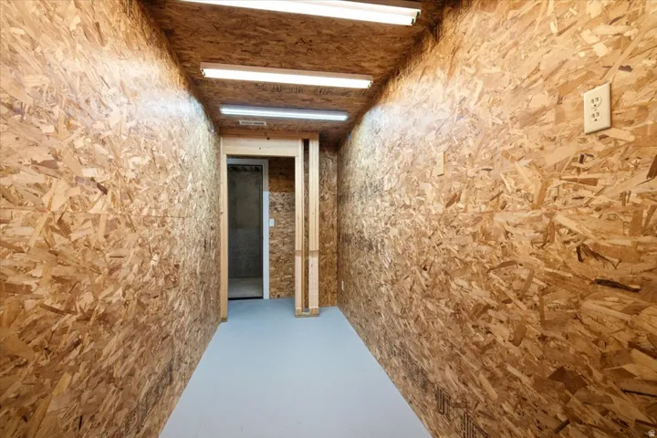 Enclosed space featuring oriented strand board walls and ceiling, a gray painted floor, and overhead fluorescent lighting