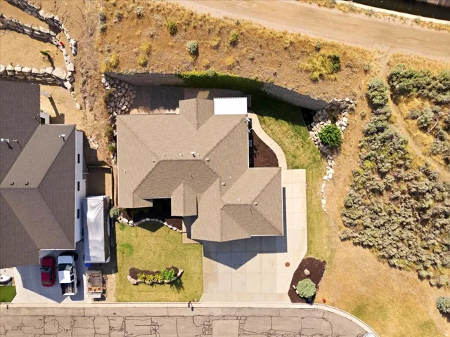 Gable roof lines featuring brown shingles, a concrete driveway, and a front lawn with a landscaped garden bed