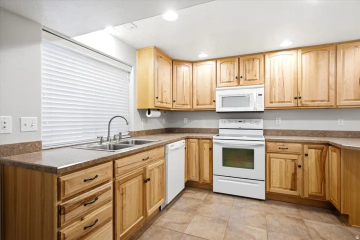 Kitchen featuring light wood cabinetry, white appliances, and a double basin stainless steel sink