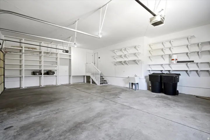 Spacious garage featuring concrete flooring, extensive built-in shelving, a utility sink, and internal staircase access