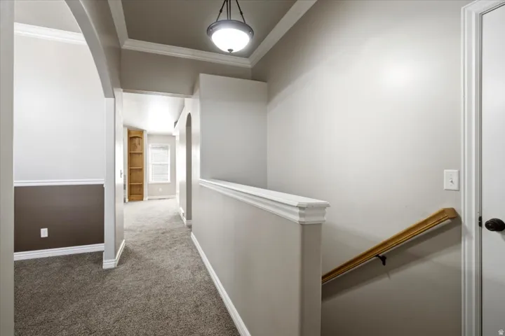Carpeted hallway featuring a built-in bookcase, arched doorway, and crown molding