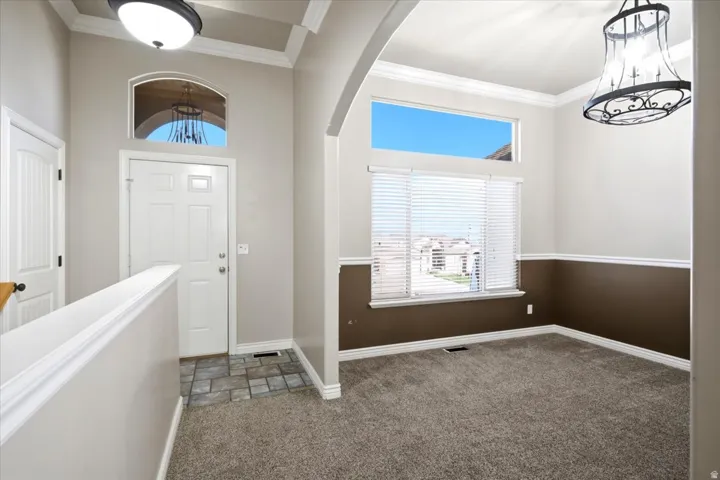 Foyer and room featuring arched entryway, crown molding, two-tone paint, and a large window with blinds