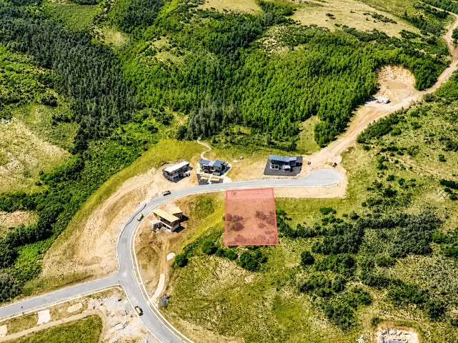 Aerial perspective showcasing a parcel of land marked in red, surrounded by lush green foliage and scattered trees