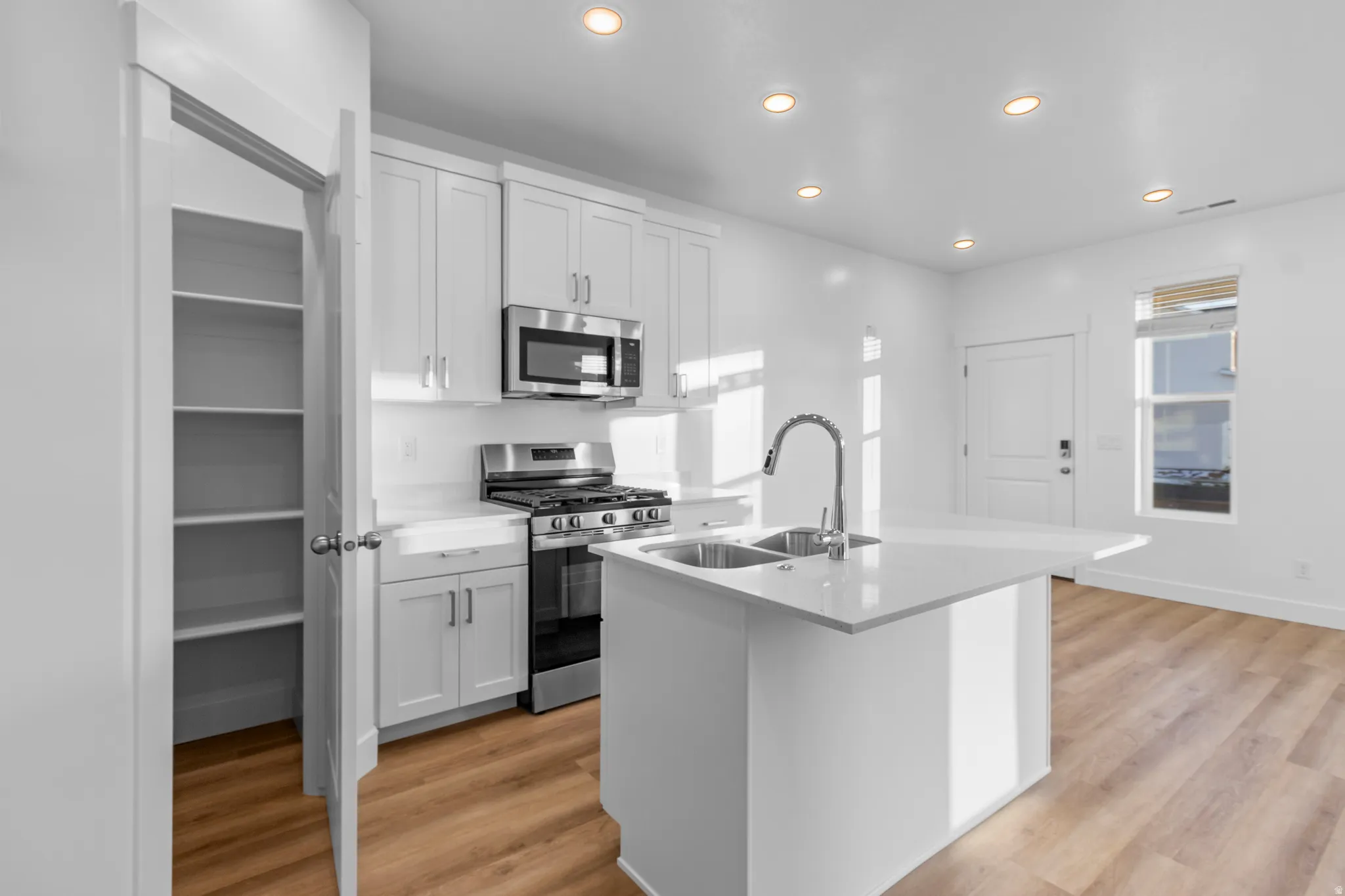 Modern kitchen featuring white cabinetry, stainless steel appliances, a center island with double sink, and wood-finish flooring