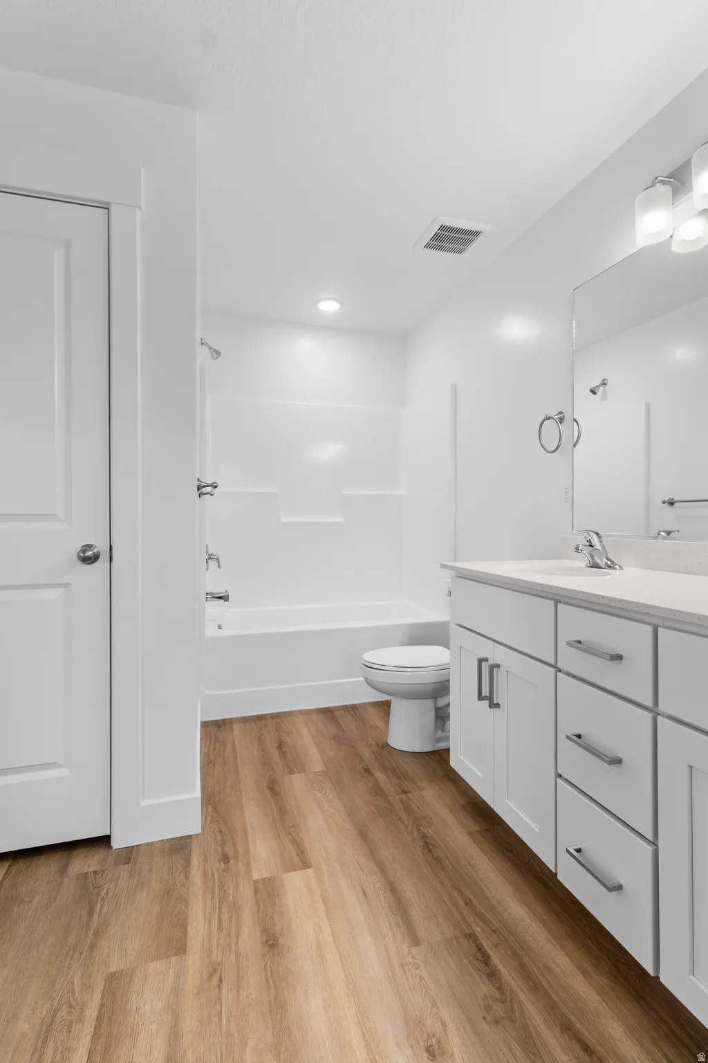 Bathroom featuring wood-finish flooring, a white vanity with brushed nickel hardware, and an integrated tub and shower unit