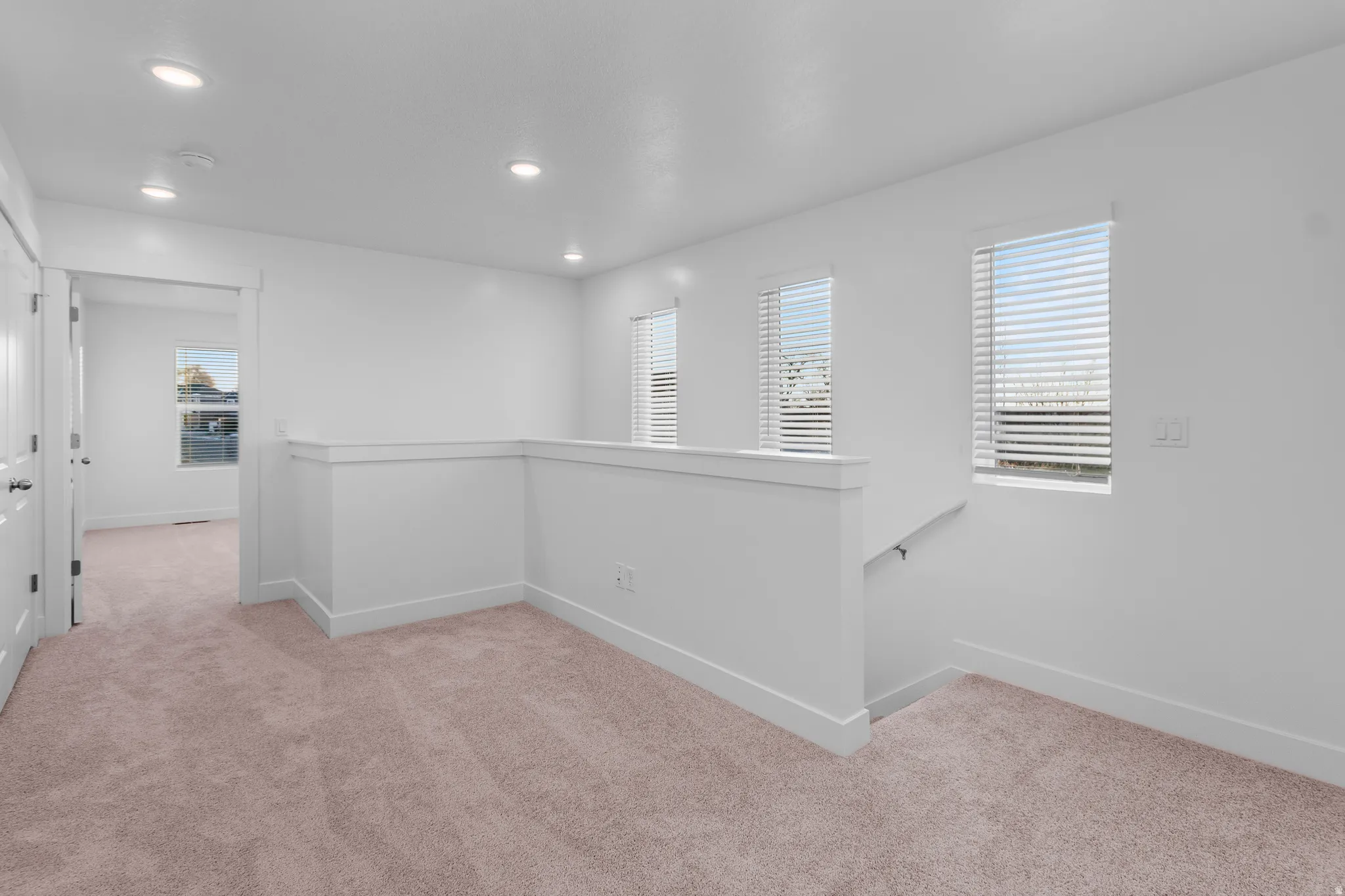 Open loft area featuring plush carpeting, white walls, recessed lighting, and multiple windows with blinds