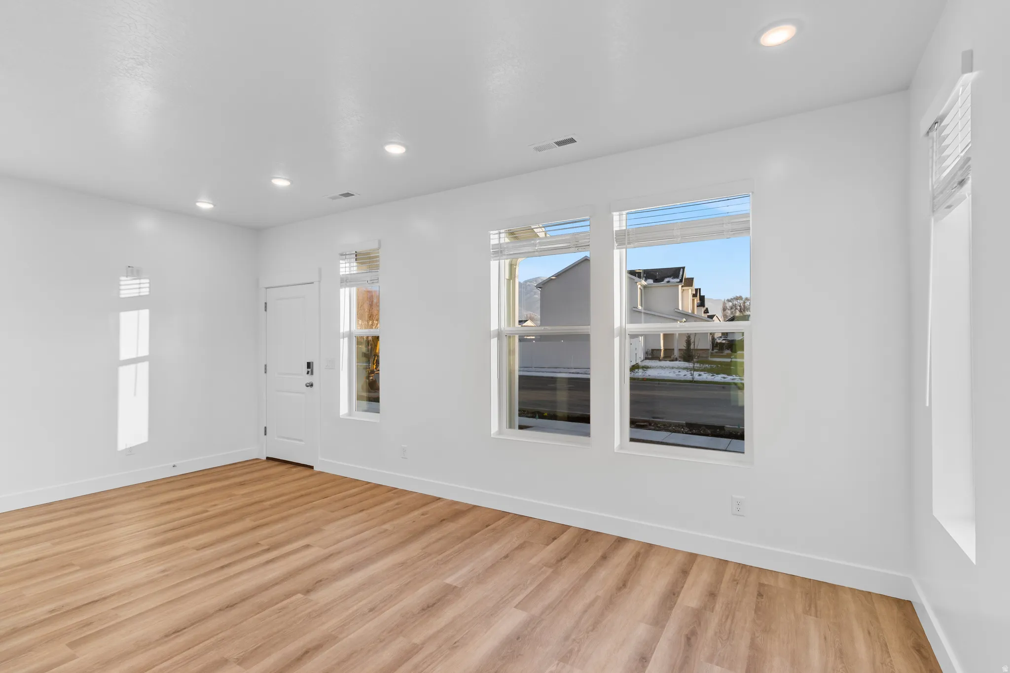 Spacious room featuring light wood-finish flooring, recessed lighting, and multiple windows