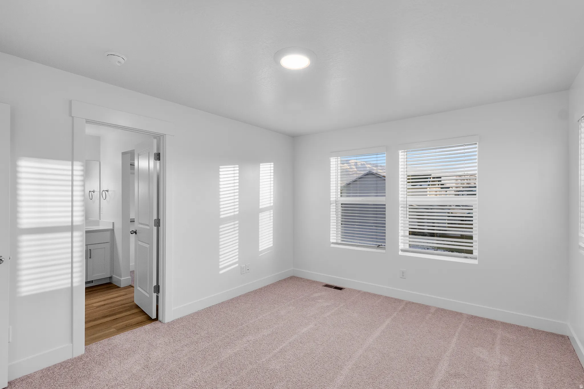 Carpeted room with white walls, featuring three windows with horizontal blinds