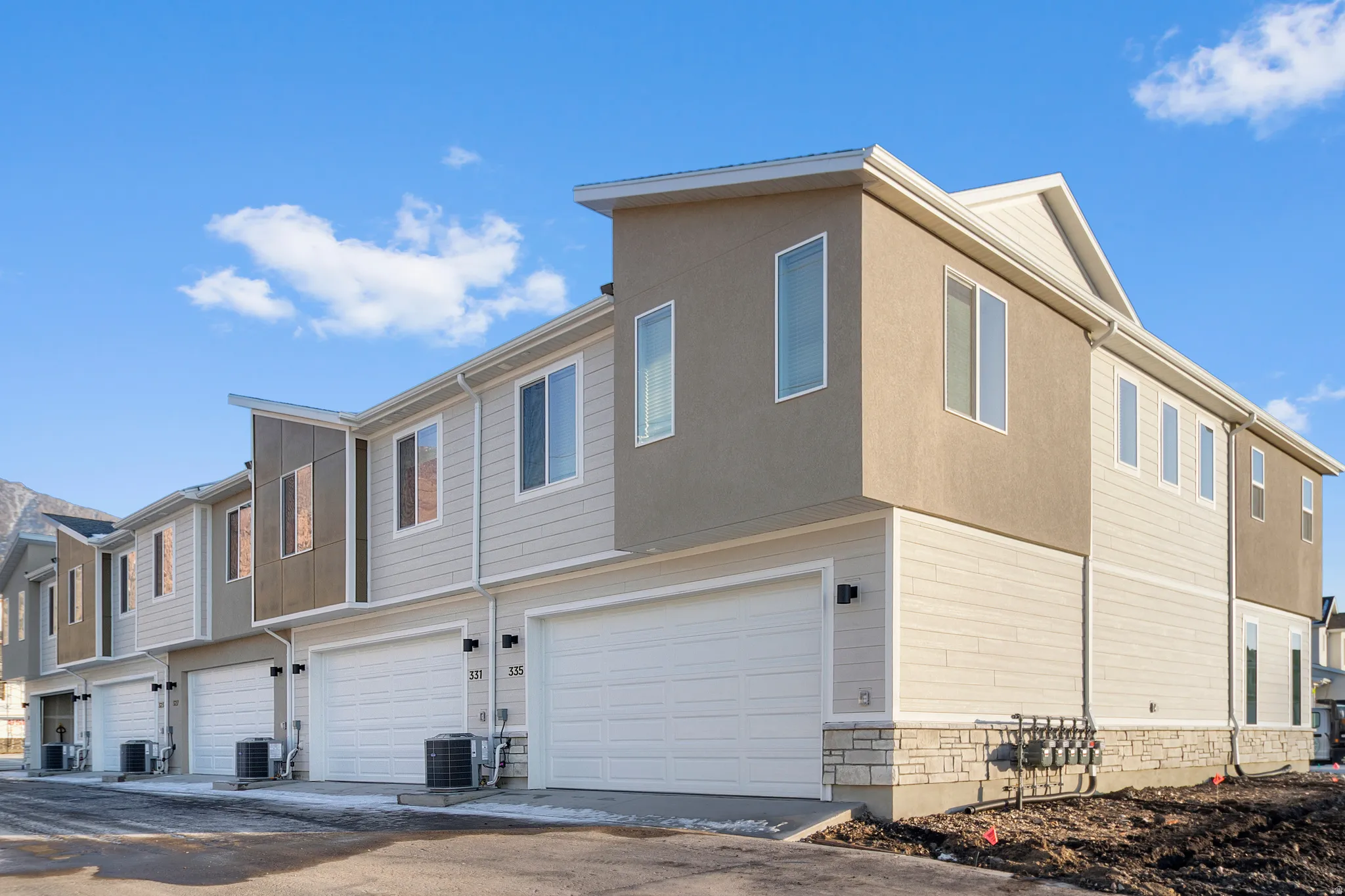 Modern townhome exterior featuring light-toned siding, stucco accents, and stone detailing