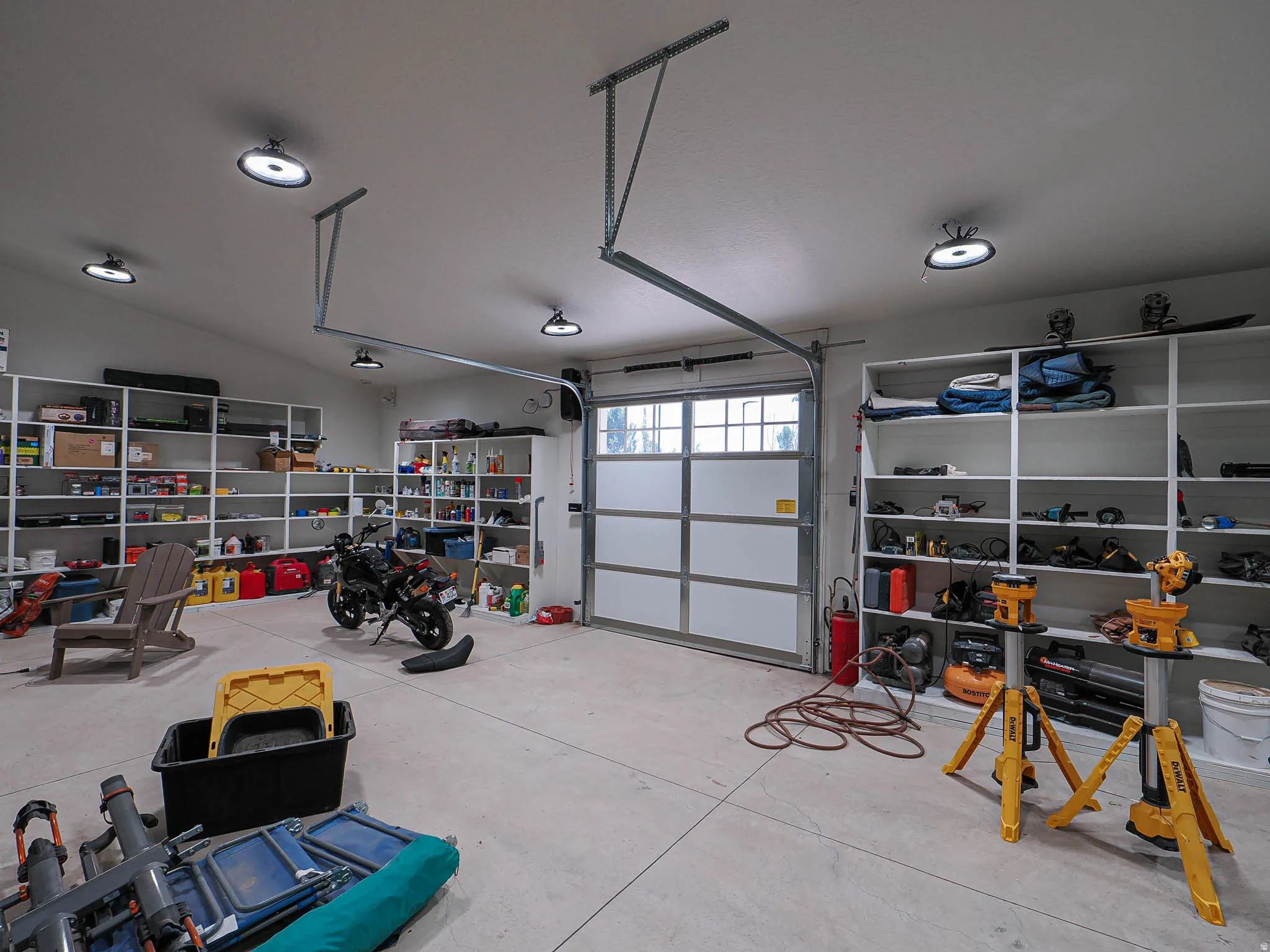 Concrete-floor garage with multiple built-in shelving units, overhead lighting, and an overhead door with frosted glass panels