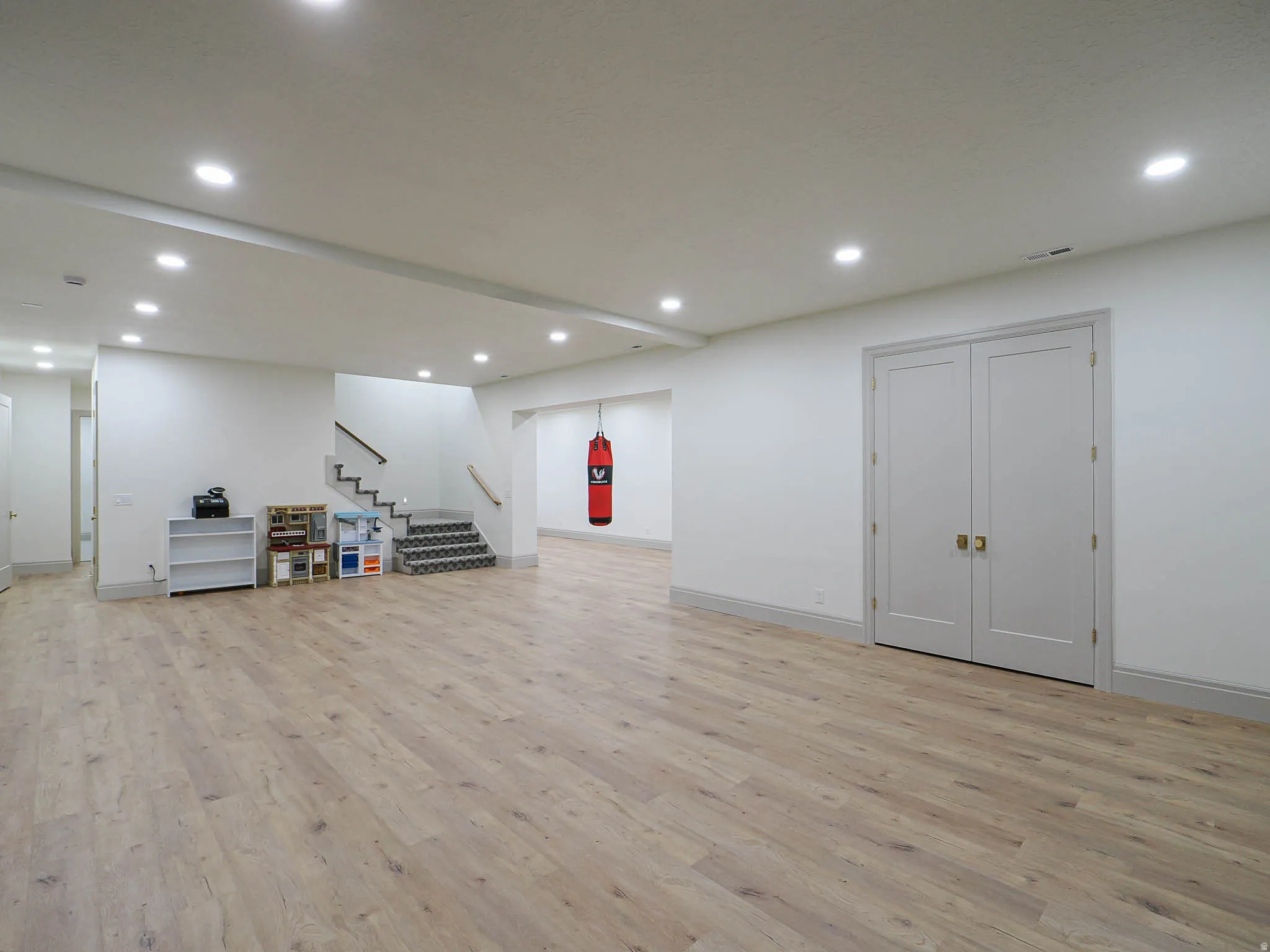 Expansive open-concept room featuring light wood-finish flooring, recessed lighting, and crisp white walls