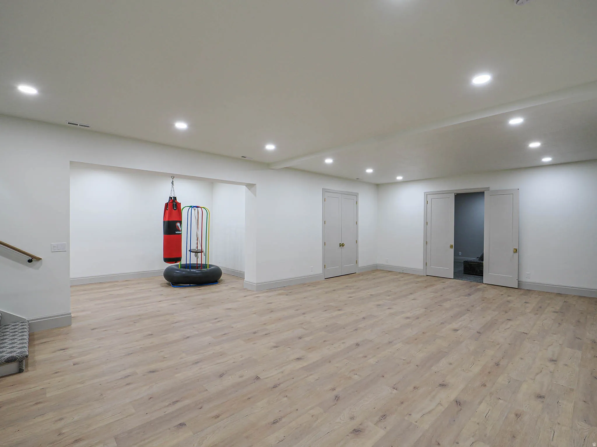 Spacious room featuring light wood-finish flooring, recessed lighting, white walls, and a substantial built-in alcove
