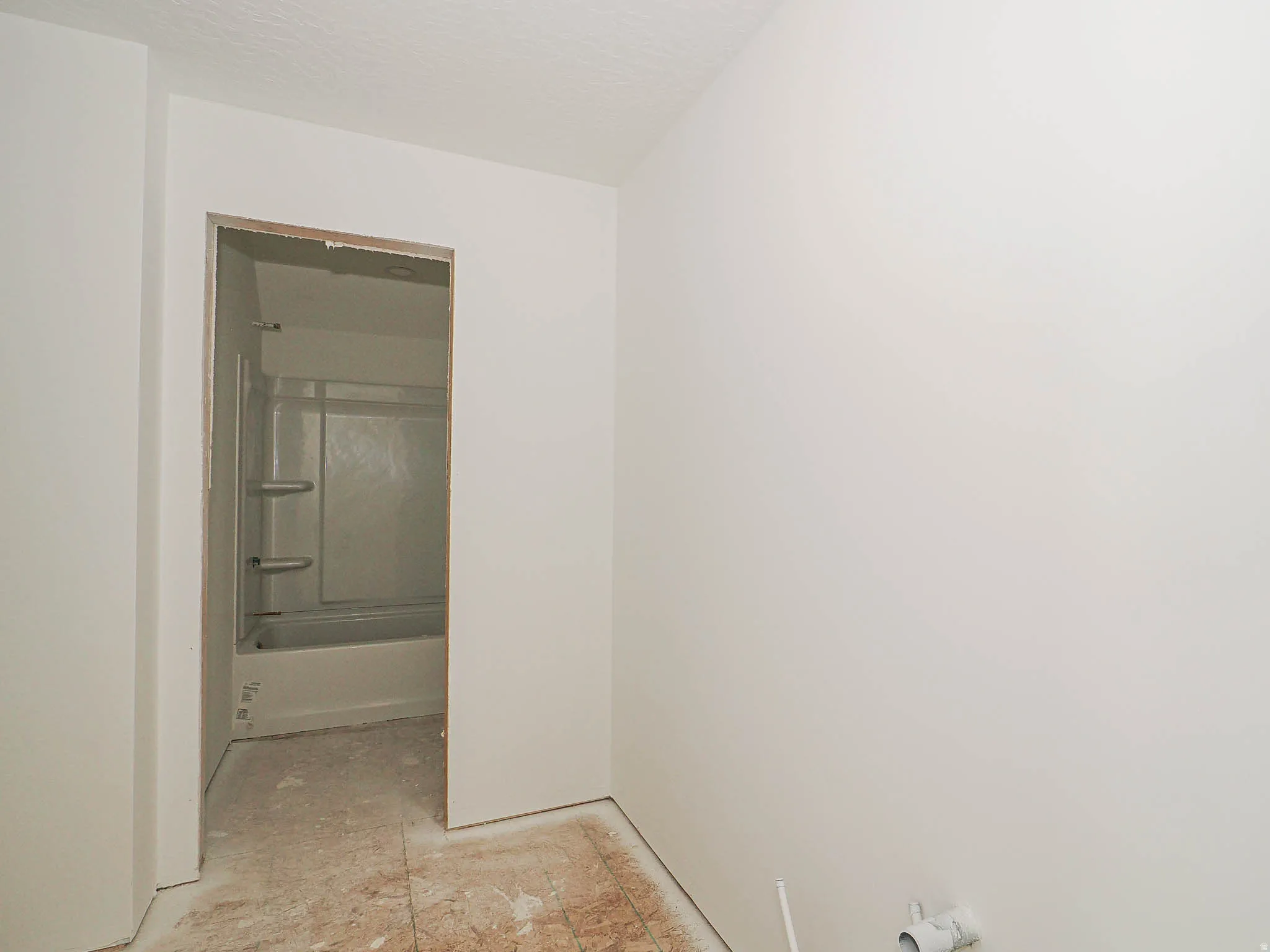 Interior space with white painted walls and an open doorway revealing a bathtub with a white surround and built-in shelving