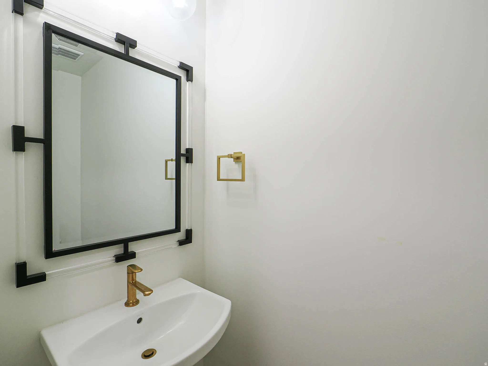 Wall-mounted sink featuring a brass-finish faucet, under-sink drain, and a coordinating brass-finish towel ring