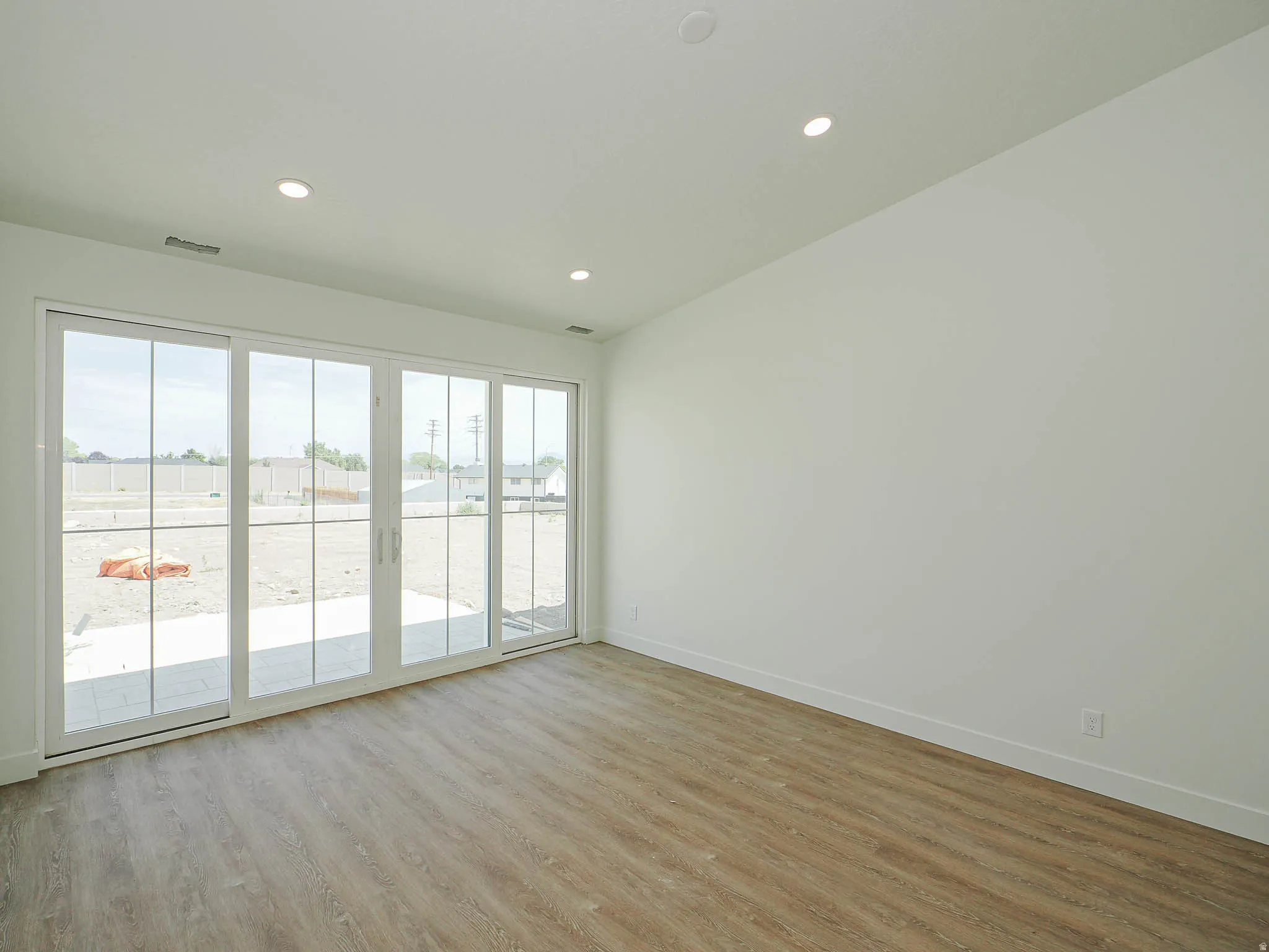 Expansive sliding glass doors, wood-finish flooring, recessed lighting, white walls, and a visible patio area