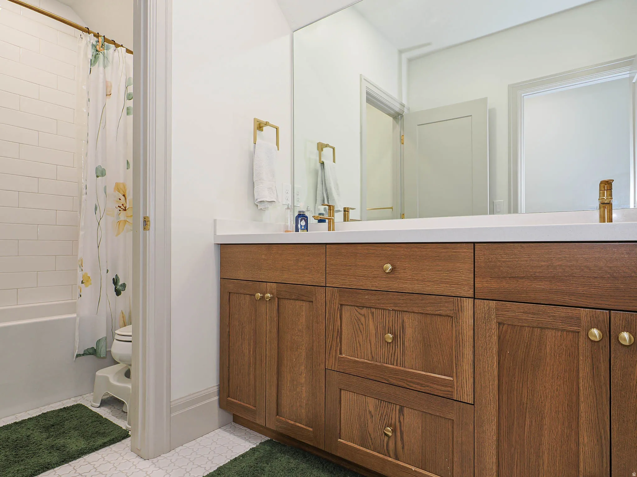 Bathroom featuring a wood-finish vanity with brass hardware, a white countertop, and a large wall-mounted mirror
