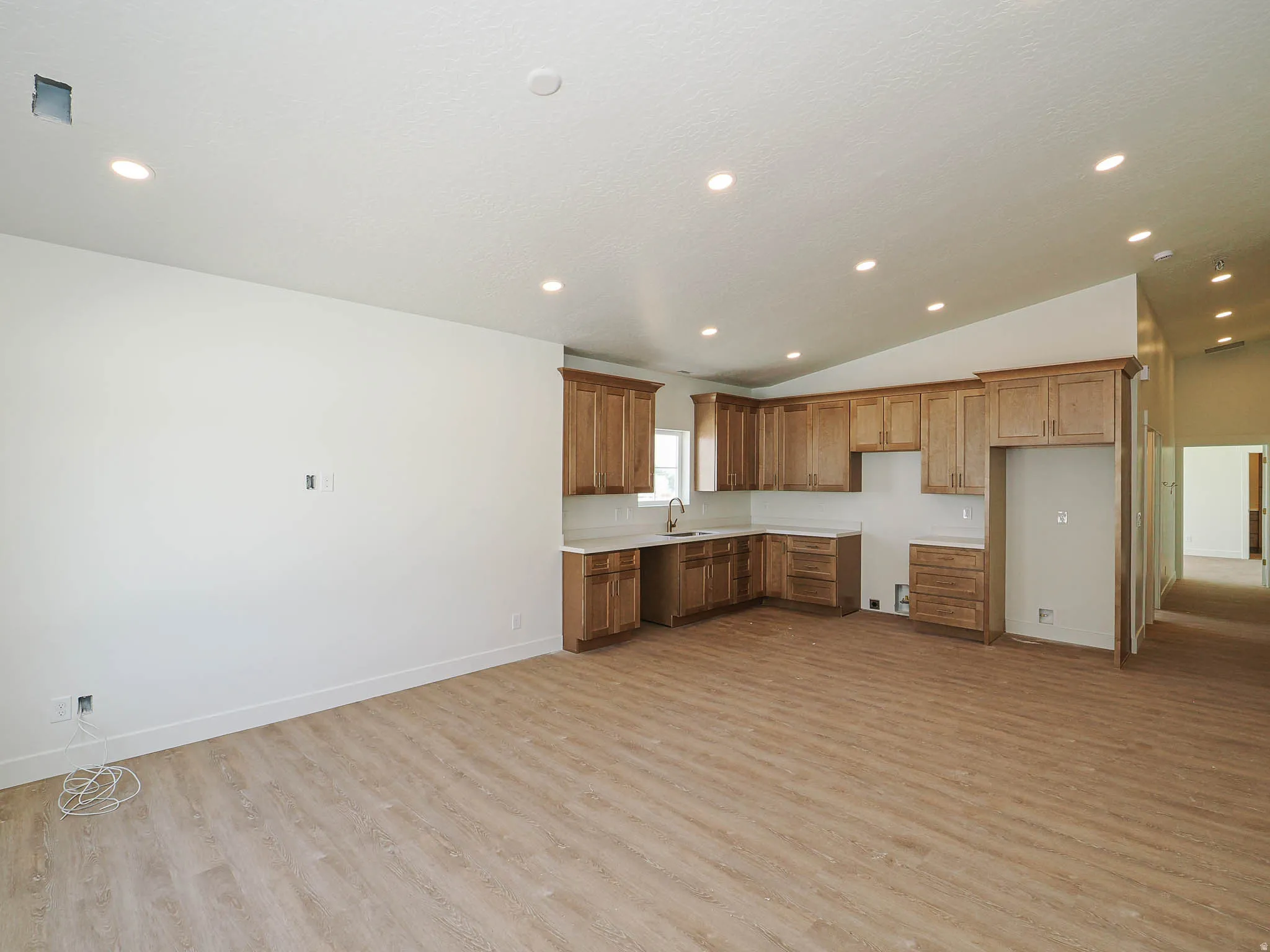 Open-concept kitchen area featuring light wood-finish flooring, vaulted ceilings with recessed lighting, custom wood cabinetry, and solid surface countertops