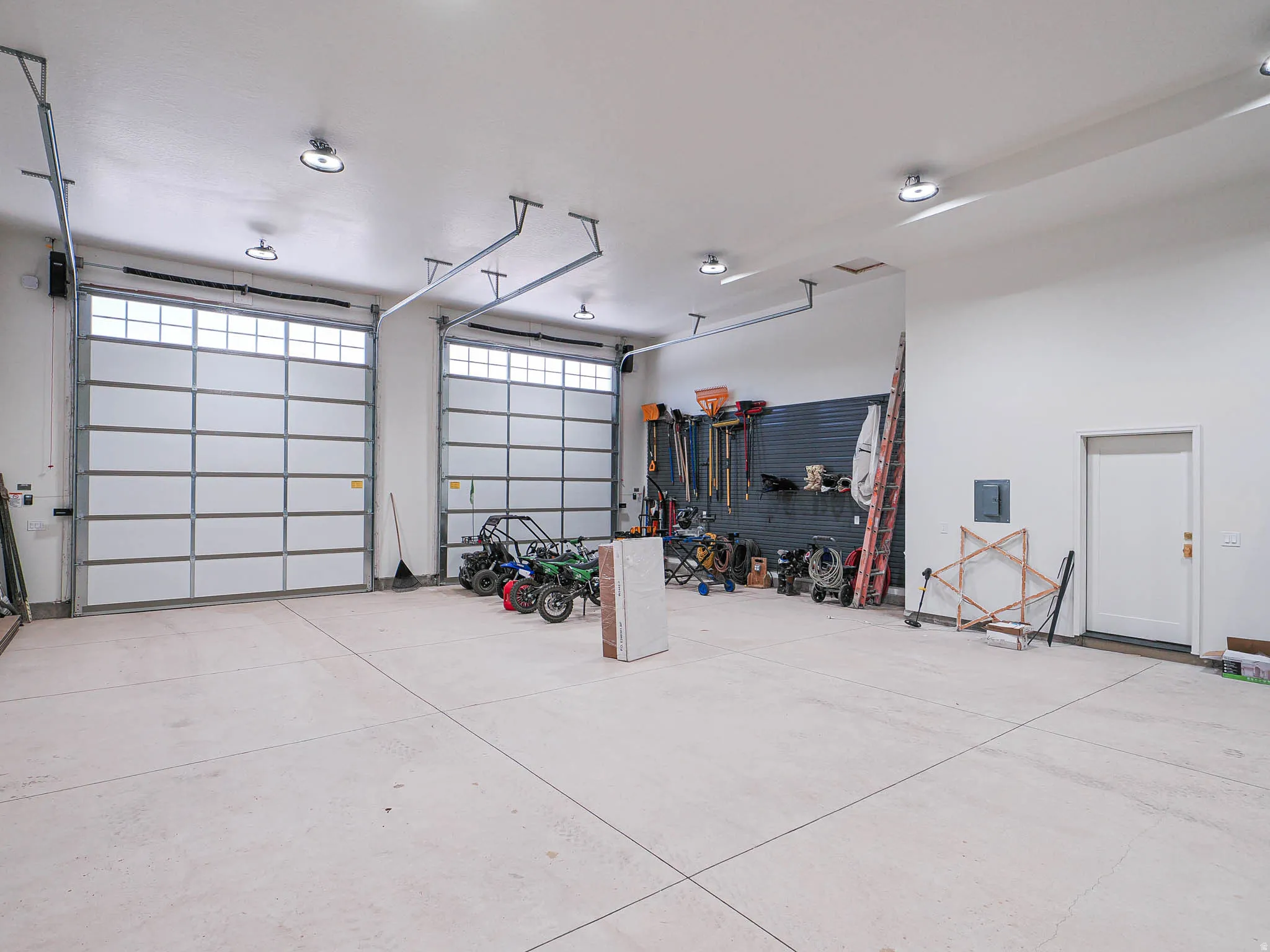 Spacious garage featuring two overhead doors with transom windows, exposed ceiling tracks, and ample overhead lighting