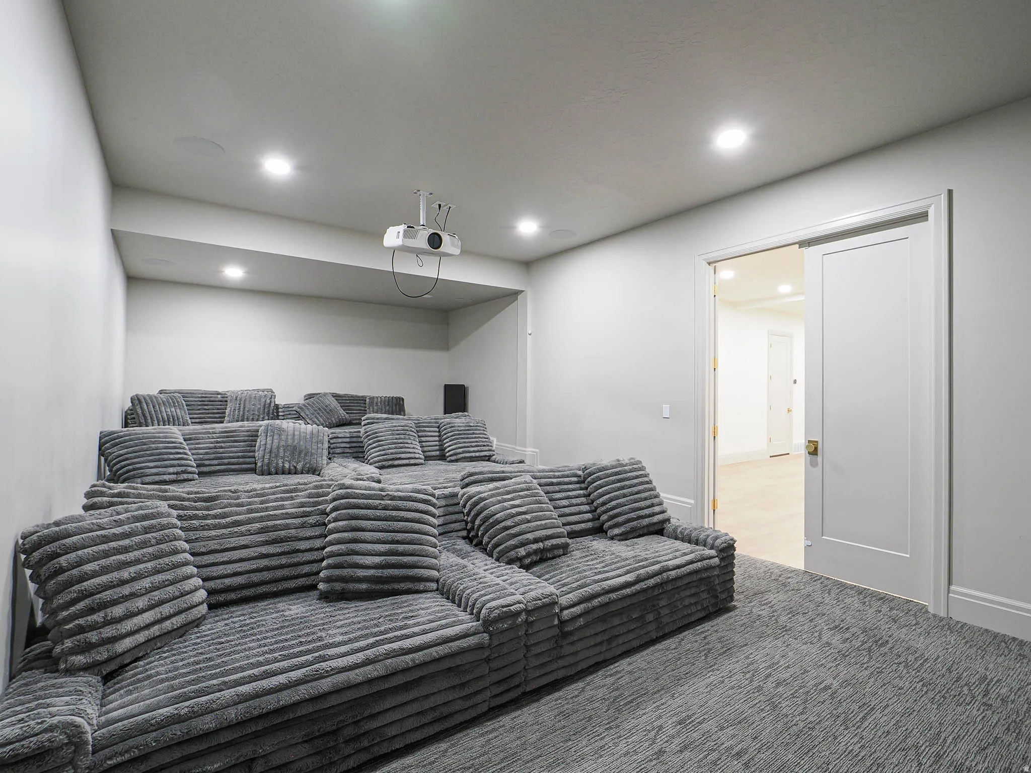 Dedicated media room featuring tiered seating, recessed lighting, a ceiling-mounted projector, and dark textured carpeting