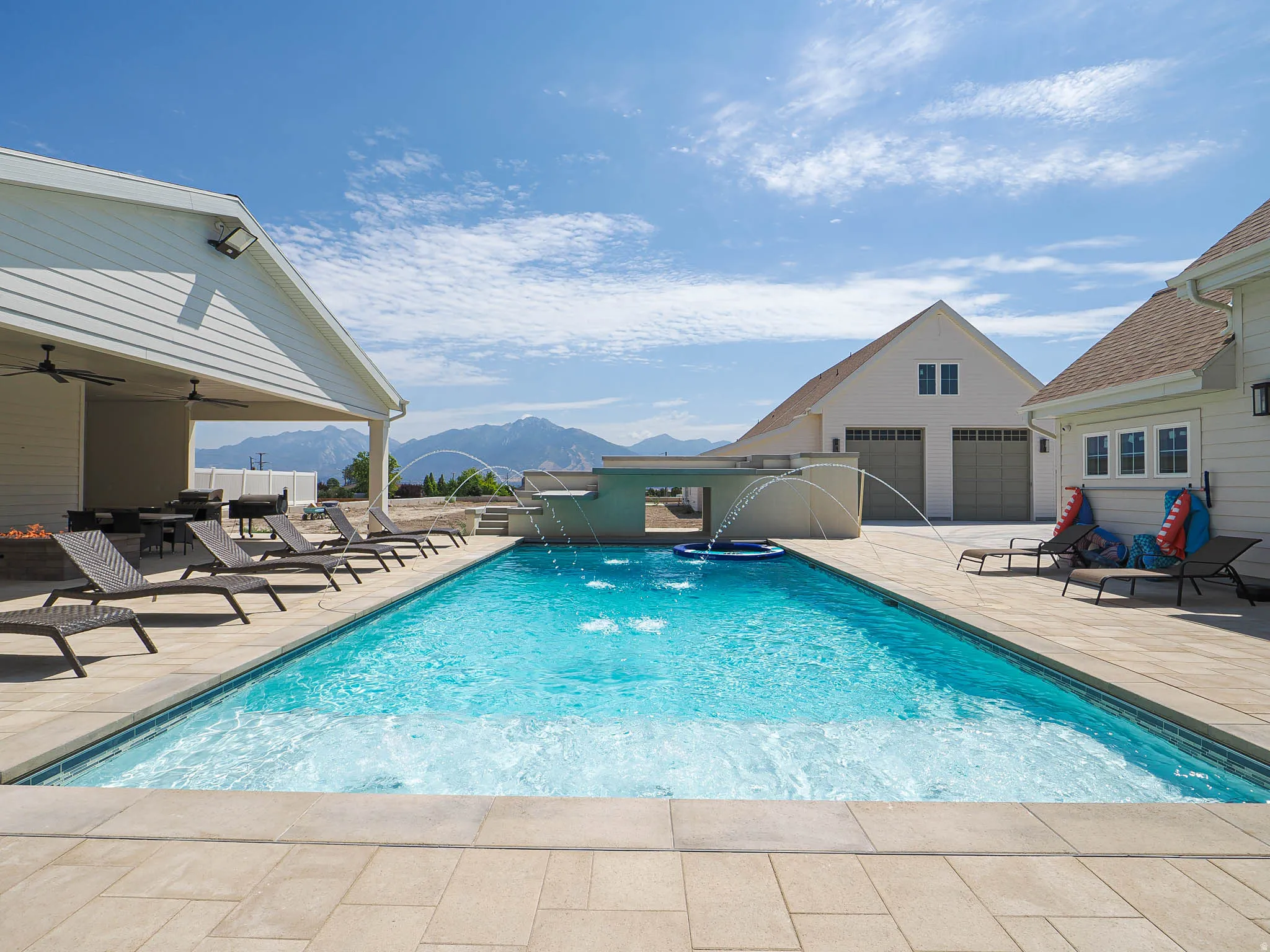 Rectangular inground swimming pool with water features surrounded by extensive paver decking