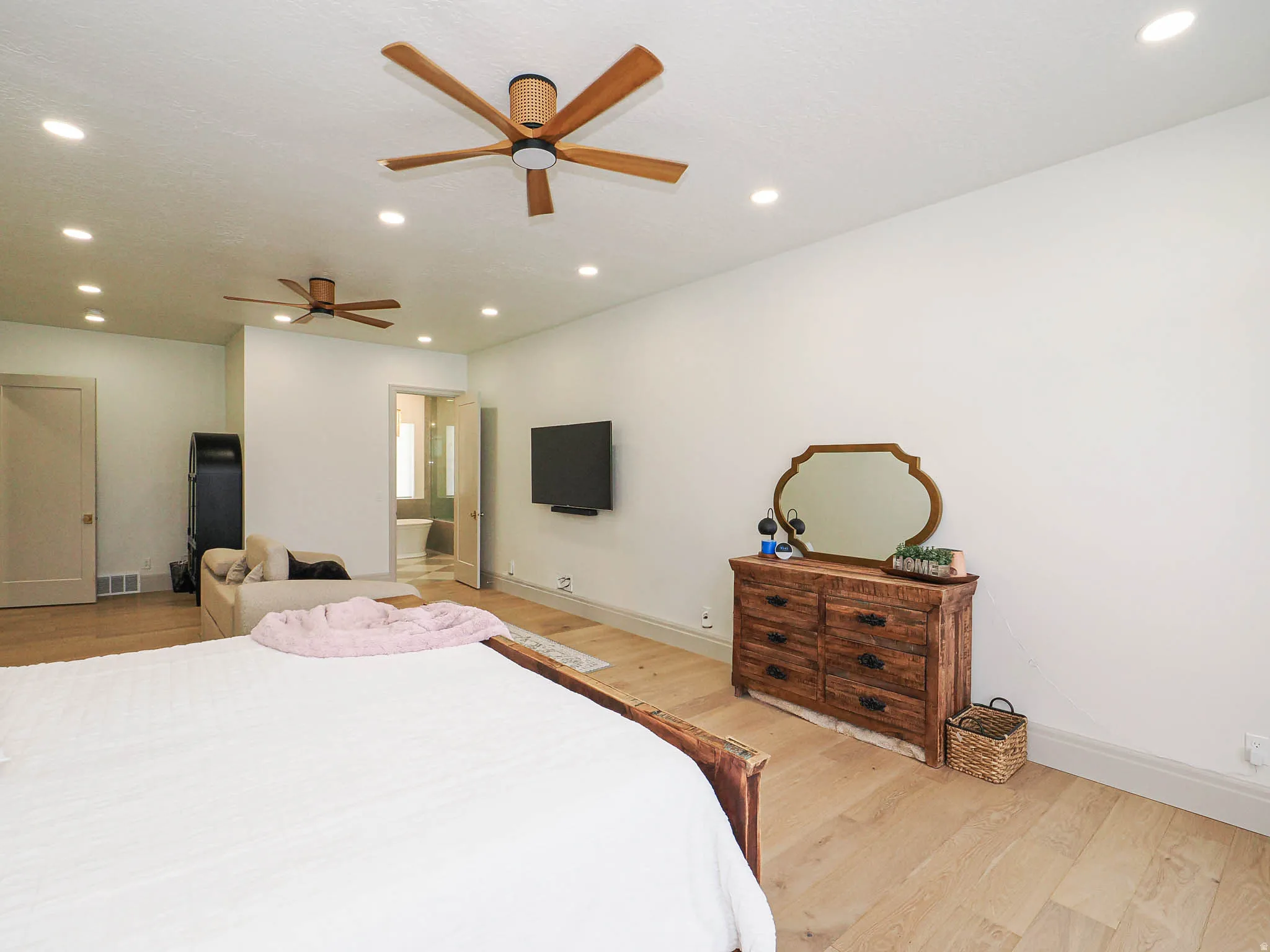 Spacious room featuring light wood-finish flooring, recessed lighting, and two ceiling fans with wood-look blades