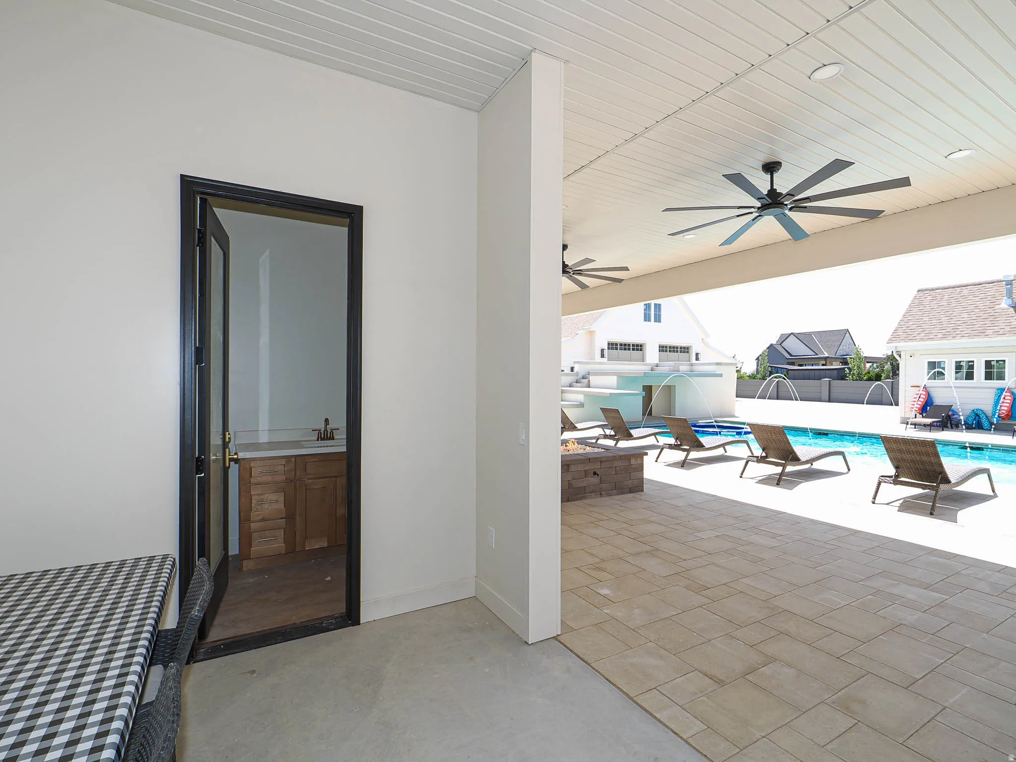 Expansive covered patio featuring a large swimming pool, paver hardscaping, dual ceiling fans, and a built-in outdoor fire pit