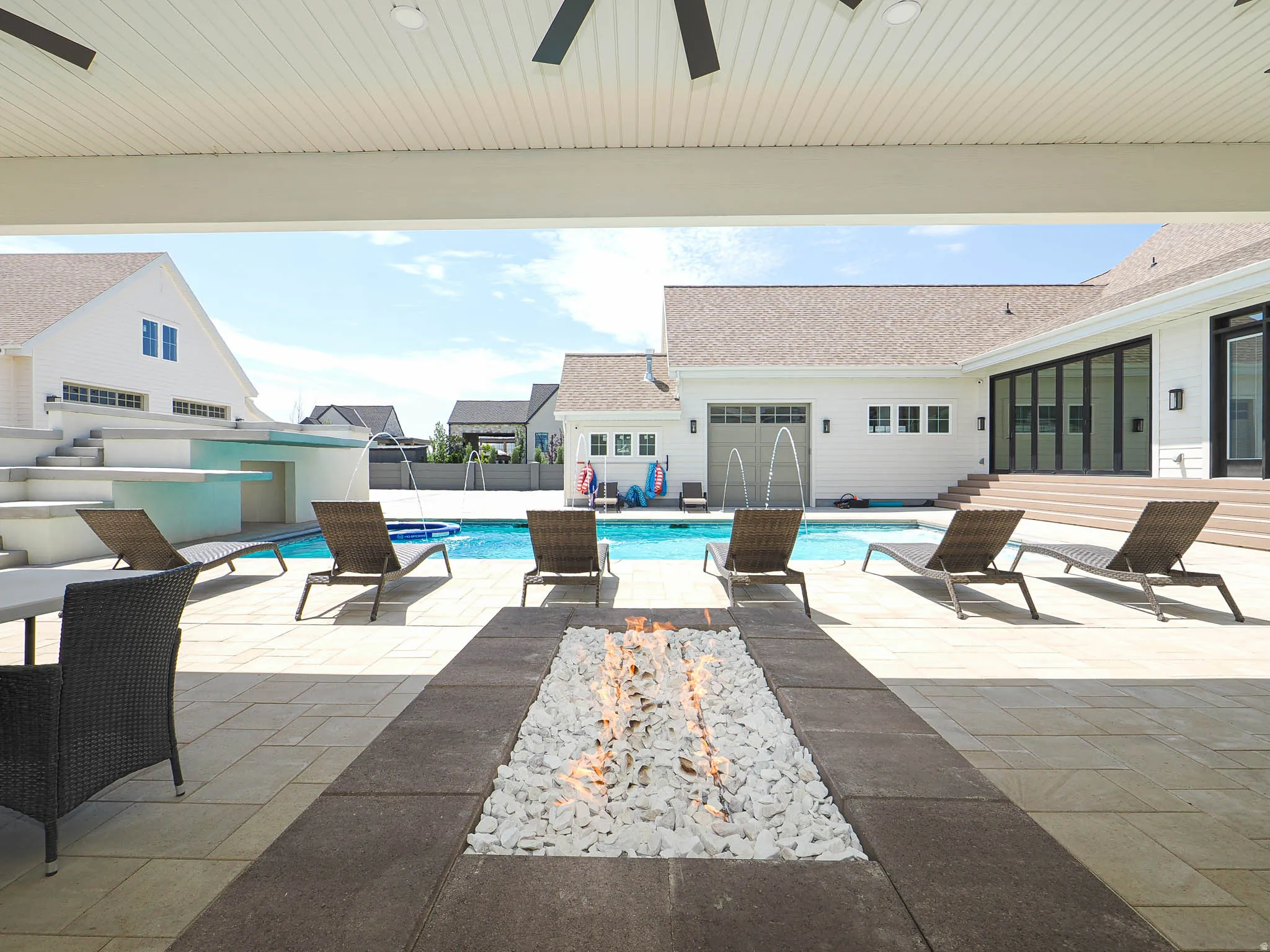 Expansive covered patio featuring a built-in fire pit, smooth ceiling with integrated fans, and a spacious paver stone surface