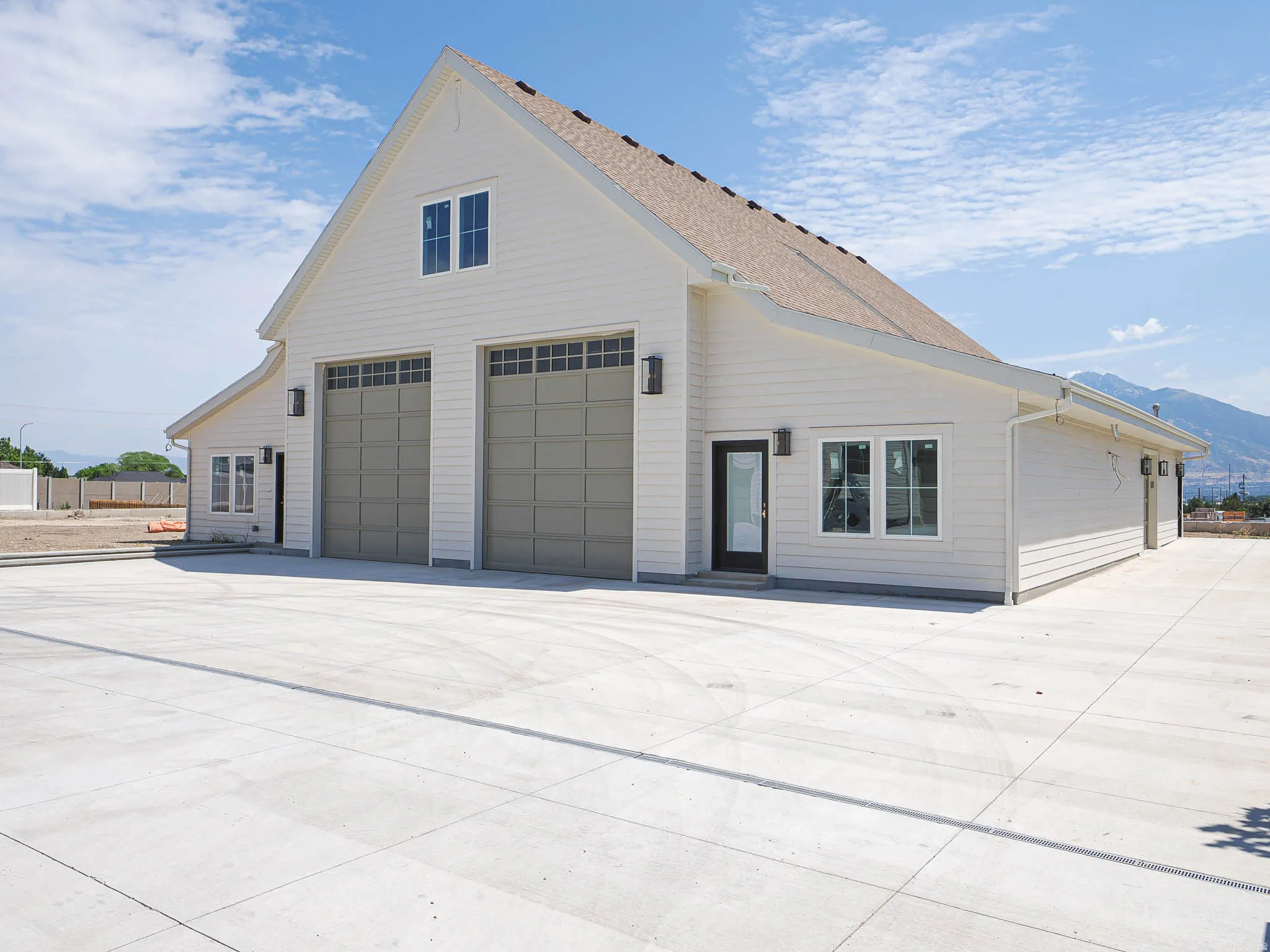Two-story structure with light-colored horizontal siding, a steeply pitched roof, and two large garage doors with upper window panels